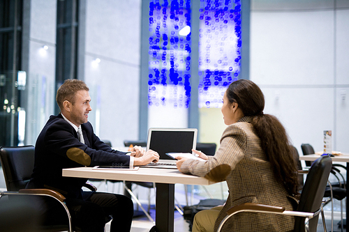 Side view portrait of two business partners, man and woman, sitting at table in cafe and discussing work