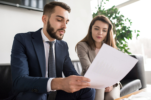 Portrait of two modern business people, man and woman, discussing documents in office, focus on handsome man in foreground