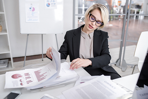 Portrait of successful blonde businesswoman discussing statistics report with colleagues looking at graphs and charts with financial data during meeting in modern office