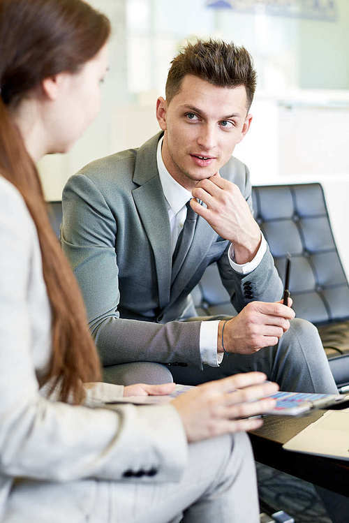 Portrait of young businessman talking to female colleague in meeting sitting at coffee table
