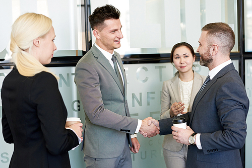 Portrait of four business partners shaking hands standing in hall of modern office building after closing beneficial deal