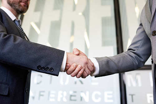 Close up of business partners shaking hands standing in hall of modern office building after closing beneficial deal