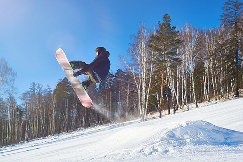 Portrait of young man performing snowboarding stunt flying high in air against clear blue sky on mountain piste, copy space