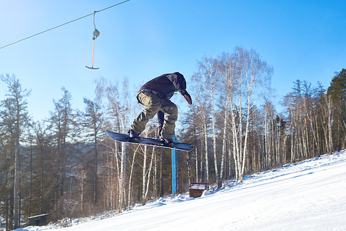 Portrait of young man performing snowboarding stunt flying high in air on mountain piste  at ski resort, copy space