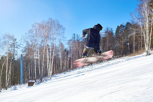 Portrait of young man performing snowboarding stunt jumping high in air and holding board backwards on mountain piste at ski resort, copy space