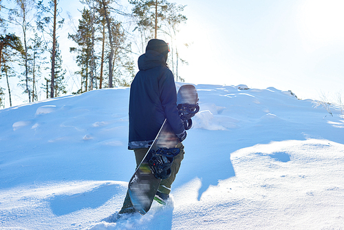 Portrait of young snowboarder running up snowy hill to go freestyle riding on wild path in the woods, copy space