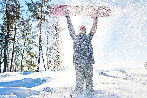 Full length portrait of young man rising up snowboard standing in shower of snowflakes enjoying sunny day in mountains, copy space