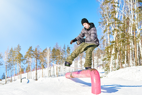 Full length portrait of young man performing snowboarding stunt sliding down metal railing in sunlight at ski resort, copy space