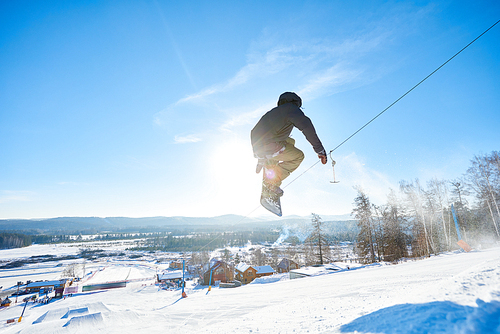 Full length action shot of young man performing snowboarding stunt jumping high in  sunlight at ski resort, copy space