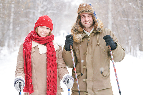 Waist up portrait of active young couple skiing in snowy winter forest on date  and smiling at camera