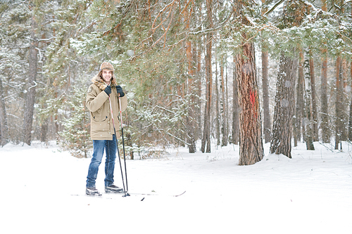 Full length portrait of happy young man smiling at camera while enjoying skiing in snowy winter forest, copy space