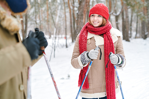 Waist up portrait of beautiful young woman smiling and looking at boyfriend while enjoying skiing in beautiful winter forest, copy space