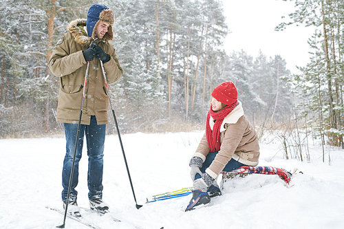 Full length portrait of active young couple skiing in winter forest focus on woman rubbing sprained ankle and looking at boyfriend, copy space