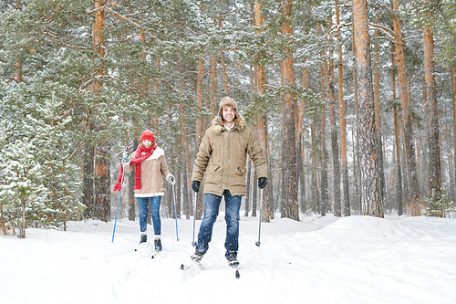 Full length portrait of modern active couple enjoying skiing in snowy winter forest during date, copy space