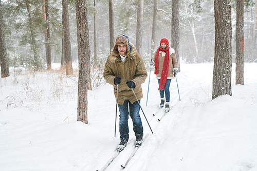 Full length portrait of modern active couple enjoying skiing in beautiful  winter forest, copy space