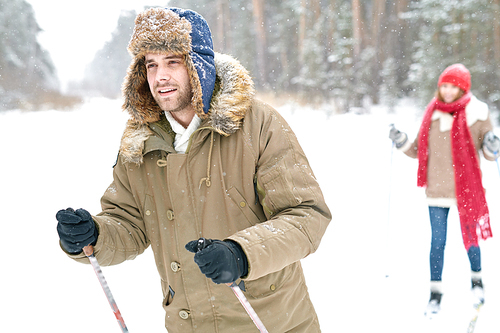 Waist up portrait of modern couple enjoying skiing in snowy winter forest, focus on handsome man in front, copy space