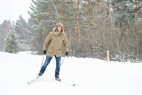 Full length portrait of handsome young man enjoying skiing in snowy winter forest, copy space