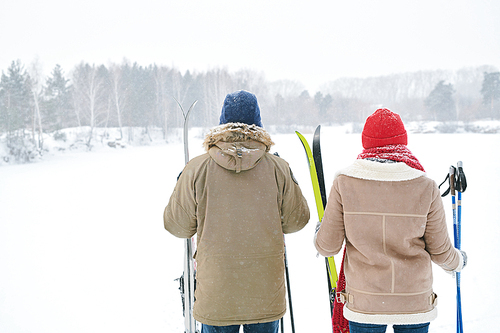 Back view portrait of active young couple looking at view of beautiful winter landscape while taking break during skiing trip, copy space