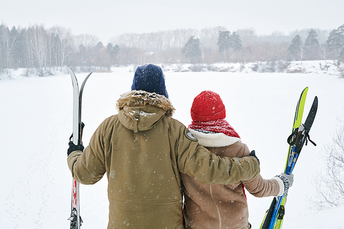 Back view portrait of loving young couple looking at view of beautiful winter landscape while taking break during skiing trip, copy space