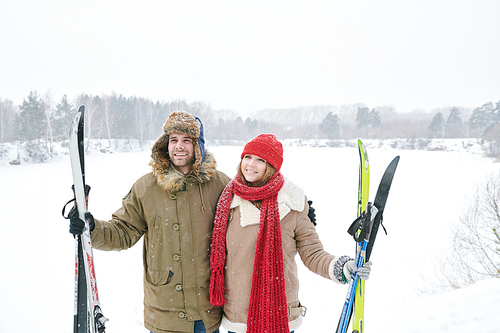 Waist up portrait of loving young couple embracing and smiling happily while taking break during skiing trip and posing against beautiful winter landscape, copy space