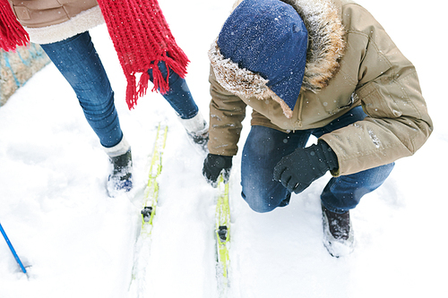 High angle portrait of young man fixing ski of his girlfriend during winter trip, copy space