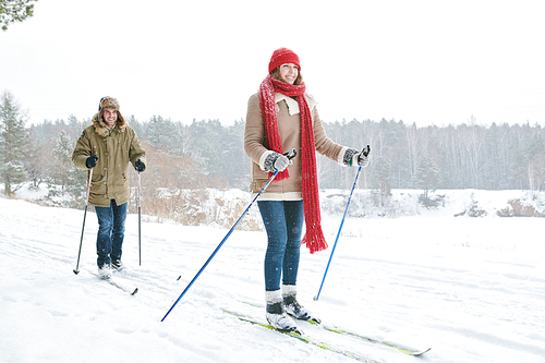 Full length portrait of active young couple enjoying skiing in snowy winter forest, focus on smiling woman in front, copy space