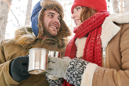 Head and shoulders portrait of loving young couple enjoying hot cocoa during date in beautiful winter forest