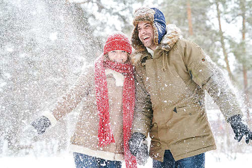 Waist up portrait of playful young couple throwing snow and smiling happily while enjoying date in beautiful winter forest, copy space