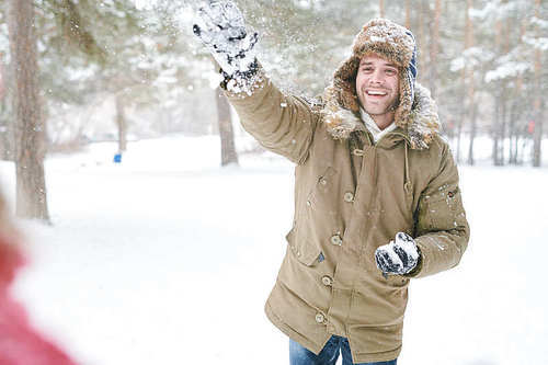 Waist up portrait of handsome young man enjoying snowball fight with friends in beautiful winter forest, copy space