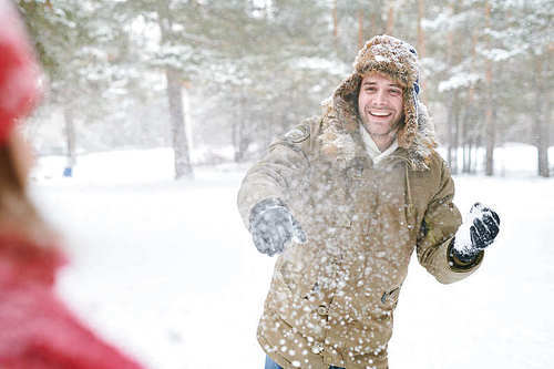 Waist up portrait of handsome young man laughing happily while enjoying snowball fight with friends in beautiful winter forest, copy space