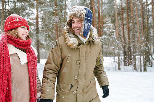 Waist up portrait of handsome young man looking at girlfriend and smiling happily while walking together through beautiful winter park, copy space