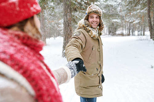 Waist up portrait of handsome young man looking at girlfriend and smiling happily while leading her through beautiful winter park, copy space