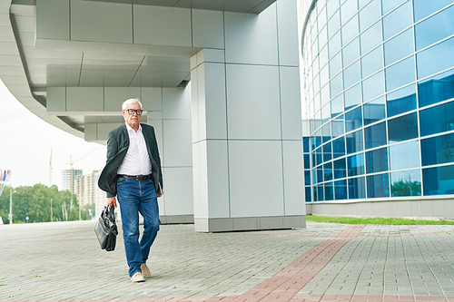 Elderly man with briefcase walking on pavement near modern office building