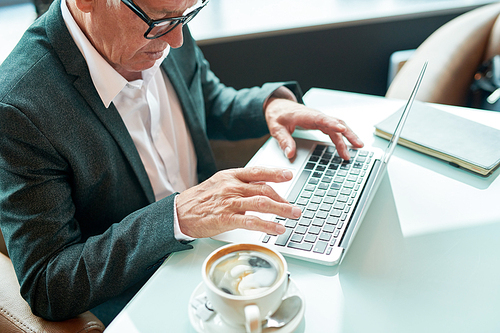 From above shot of crop entrepreneur sitting at cafe table near cup of fresh coffee and browsing laptop