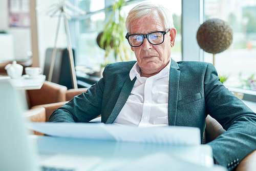 Portrait of contemporary senior businessman reading documents while working in cafe , copy space
