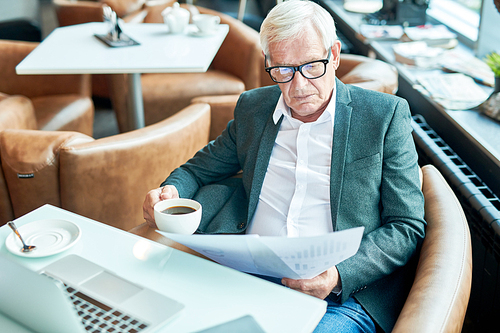 High angle portrait of contemporary senior businessman reading documents while working in cafe during coffee break , copy space