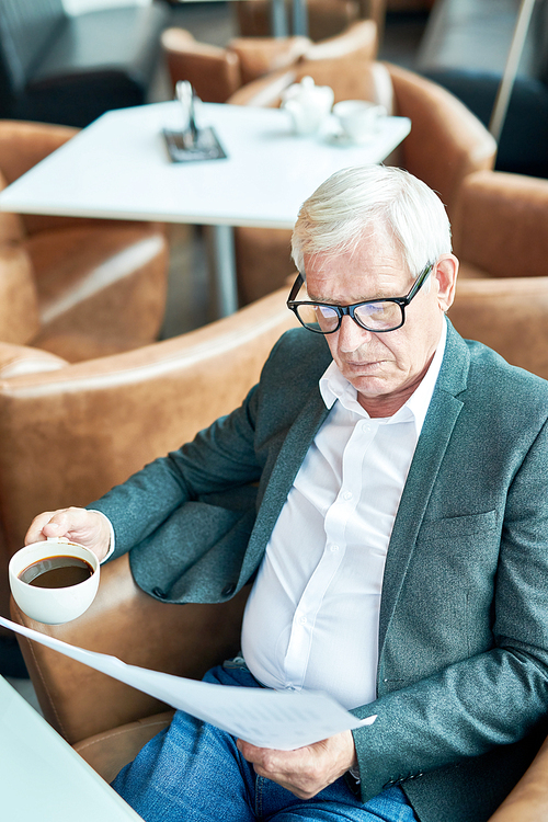 High angle portrait of contemporary senior businessman reading documents while working in cafe during coffee break