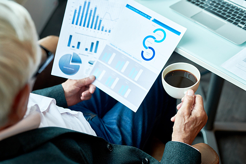 High angle portrait of unrecognizable senior businessman reading documents while working in cafe during coffee break , copy space