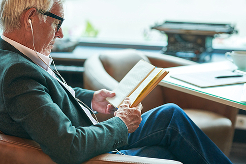 Side view portrait of successful senior businessman reading book in cafe while relaxing during coffee break, copy space