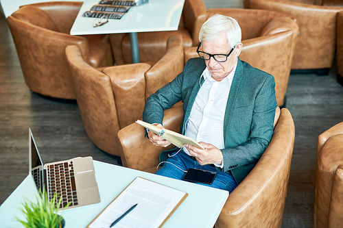 High angle portrait of successful senior businessman reading book in cafe while relaxing during coffee break, copy space