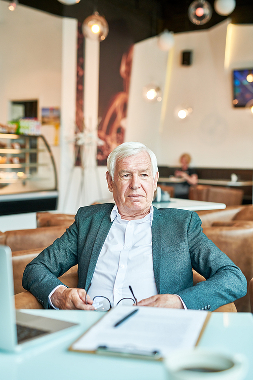 Portrait of contemporary senior businessman looking away pensively while working at table in cafe during coffee break