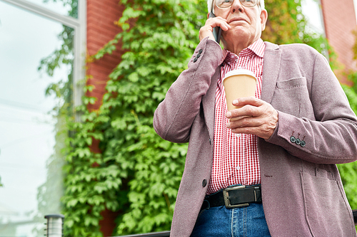 Mid section portrait of modern senior businessman speaking by smartphone standing on terrace outdoors and holding paper coffee cup, copy space