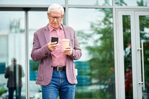 Portrait of modern senior businessman using smartphone standing on terrace outdoors and holding coffee cup, copy space
