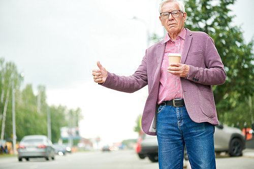 Portrait of modern senior businessman calling taxi standing by road in city, copy space