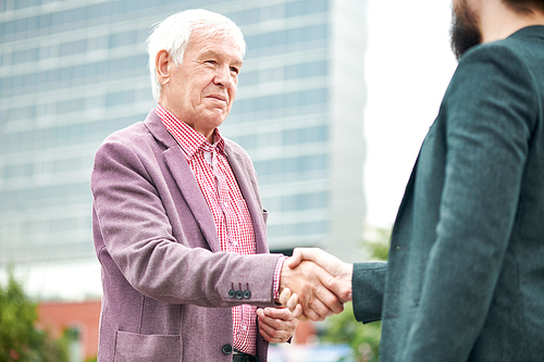 Waist up portrait of successful senior businessman shaking hands with partner outdoors, copy space