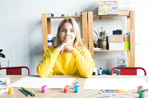 Portrait of smiling young woman sitting at the table in art class and ...