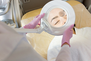 Close up of unrecognizable cosmetologist inspecting skin of young woman before beauty treatments