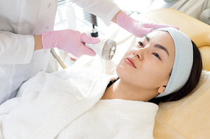 Portrait of pretty Asian woman enjoying facial care in cosmetologist office, copy space