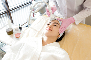 High angle portrait of pretty Asian woman enjoying facial care in cosmetologist office, copy space