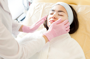 Portrait of unrecognizable cosmetologist applying refreshing eye mask to face of beautiful young woman performing beauty treatment